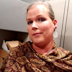 A woman with short hair, looking directly at the camera with a slight smile, wearing a floral shawl.