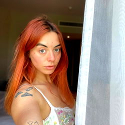 A model for OnlyFans with a striking red hair and tattoos, showcasing her unique style in the UK.