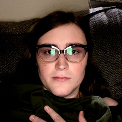 A person lying down with glasses and a neutral expression