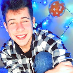 Handsome Male in Blue Shirt and Jeans, Aged 21, Sitting by String Lights with Smile