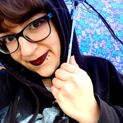 An individual posing in front of a blue umbrella under a rainy sky