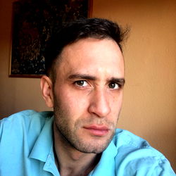 A man with a beard and mustache looking directly at the camera with an intense gaze.