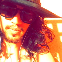 Ade, a singer with long hair and glasses, relaxed on a red bench.