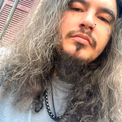 Jerrod Money Cook, A Long-Haired Man with Beard, Necklace and Tattoos, Smiling for the Camera.