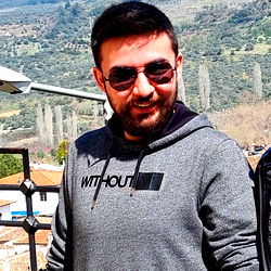 Barış, a young man standing with his hands in pockets, looking at the camera with a slight smile and sunglasses.