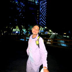 A young man captured in an urban night setting, with a cityscape and the lights of a lit bridge in the background.
