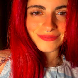 Red-haired individual with a necklace and earring, against a blurred background