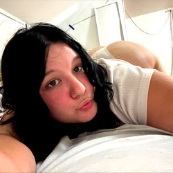 A woman lying down on a bed, smiling at the camera.