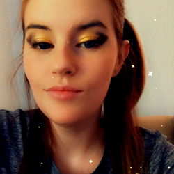 A woman with a striking gold eye shadow and hair in a ponytail