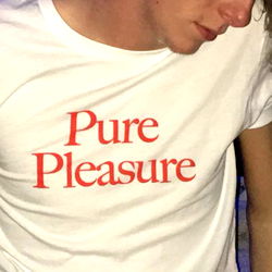 Model James Dacus in a White T-Shirt and Pure Pleasure Shirt, Standing Against the Bed