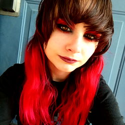 Zelda, a young model with striking red hair and dramatic eye makeup. She is wearing a black t-shirt and has a serious expression on her face.