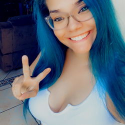 Rochelle Rodriguez, a 28 year old female with vibrant blue hair and a cheerful smile posing on her OnlyFans.