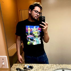 A young man with glasses, standing in a bathroom, holding a smartphone.
