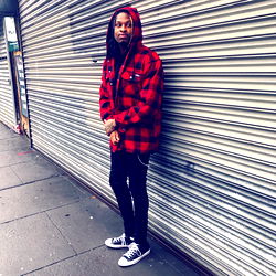 Marcel Ke’ Von, a Michigan-based model, poses confidently against a shuttered storefront in his red hoodie and jeans.