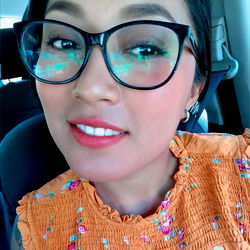 A vibrant street style image with a smiling woman in sunglasses, posing for the camera. Her outfit is casual and colorful.