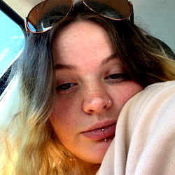 A woman in a car, resting her head on her arm with sunglasses on her head.