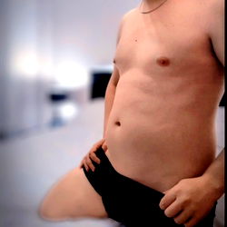 Aru 🔥, a hot Onlyfans model posing in a bedroom setting. He's shirtless, wearing black boxer shorts.