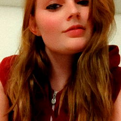 Red-haired model in a red top with a hoodie, posing for a selfie