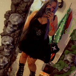 Gothic-style model posing in front of a mirror with a skull and crossbones backdrop