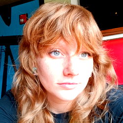 Allis Kittyqueen, a Texas model with striking red hair and expressive eyes, captured in this candid moment. Her outfit suggests a casual yet chic style.