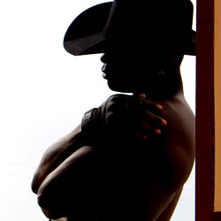 Model DUSK in Western-style attire, standing near a door with a red frame, exuding a poised and mysterious demeanor.