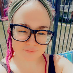 A woman wearing a colorful headband and glasses, with braided hair and a nose ring. She's standing by a pool. OnlyFans model Sonya