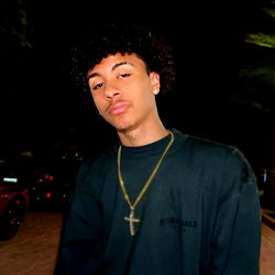 Adriel from New Jersey, pose for the camera with a focused gaze and gold chain necklace.