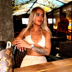 Ella Raye at a restaurant, posing in a blue dress with white accessories