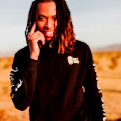 Alex Varsity in a Stylish Outfit Standing in Desert Landscape