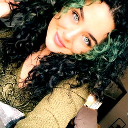 Miya, a young model in a green sweater with curly hair, smiling and looking to the left. The image is slightly blurry.