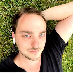 A young man resting on the grass with a slight smile.