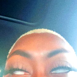 Stylized close-up portrait of a person with shaved head and vibrant eye makeup.