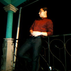 Casually Dressed Young Man Standing on Balcony at Night