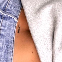 Fashion-forward female model in crop top and denim shorts, showcasing her tattoo