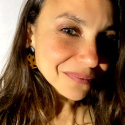 A woman with her eyes closed, smiling gently. She has dark hair and is wearing a black top with a floral pattern.