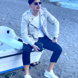 Stylish Model Sitting on Beach with Boat and Sand