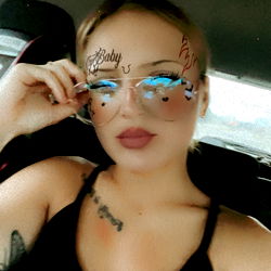 Amber from North Carolina in a blue eyeliner and black sunglasses, showcasing her tattooed arm.
