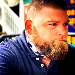 Man with a beard and mustache, wearing a blue shirt and sunglasses on his head.