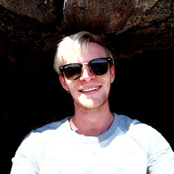 A young man from Houston, Texas. Smiling and posing for the camera in front of a rock wall.