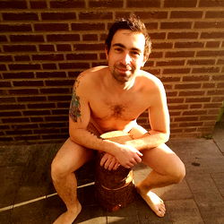 Shirtless man sitting on a stool in front of a brick wall