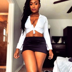 Jade, an OnlyFans model, poses for a selfie in her bedroom. She's wearing a black skirt and a white top.