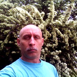 A man standing in front of a tree with white flowers and posing for a photo