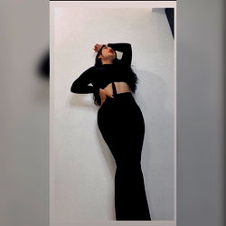 Model in Black Outfit Striking a Pose on a Plain Wall