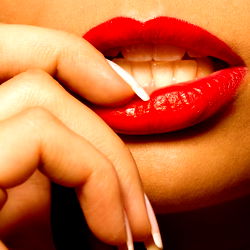 Intense Abie, with glossy red lips and a seductive gaze, captured in a candid moment of applying lipstick.