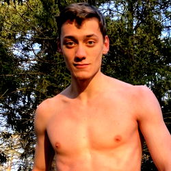 Shirtless model posing outdoors in a wooded area
