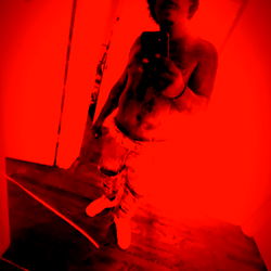 Red-tinted, artistic photo of a shirtless man with a camera in his hand