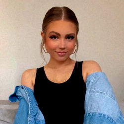 Beautiful Andrea poses confidently in a denim jacket, showcasing her makeup and hairstyle against a neutral backdrop