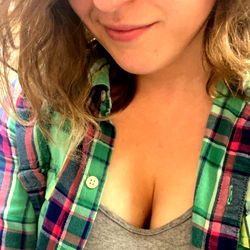 A confident Amelia Meundava, showcasing her plaid shirt and glasses, in a casual pose.