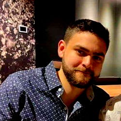 A young man with a beard in a restaurant setting, smiling and looking towards the camera