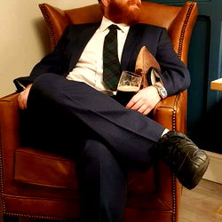 Andy, a stylish man in a suit and tie, seated on a chair.